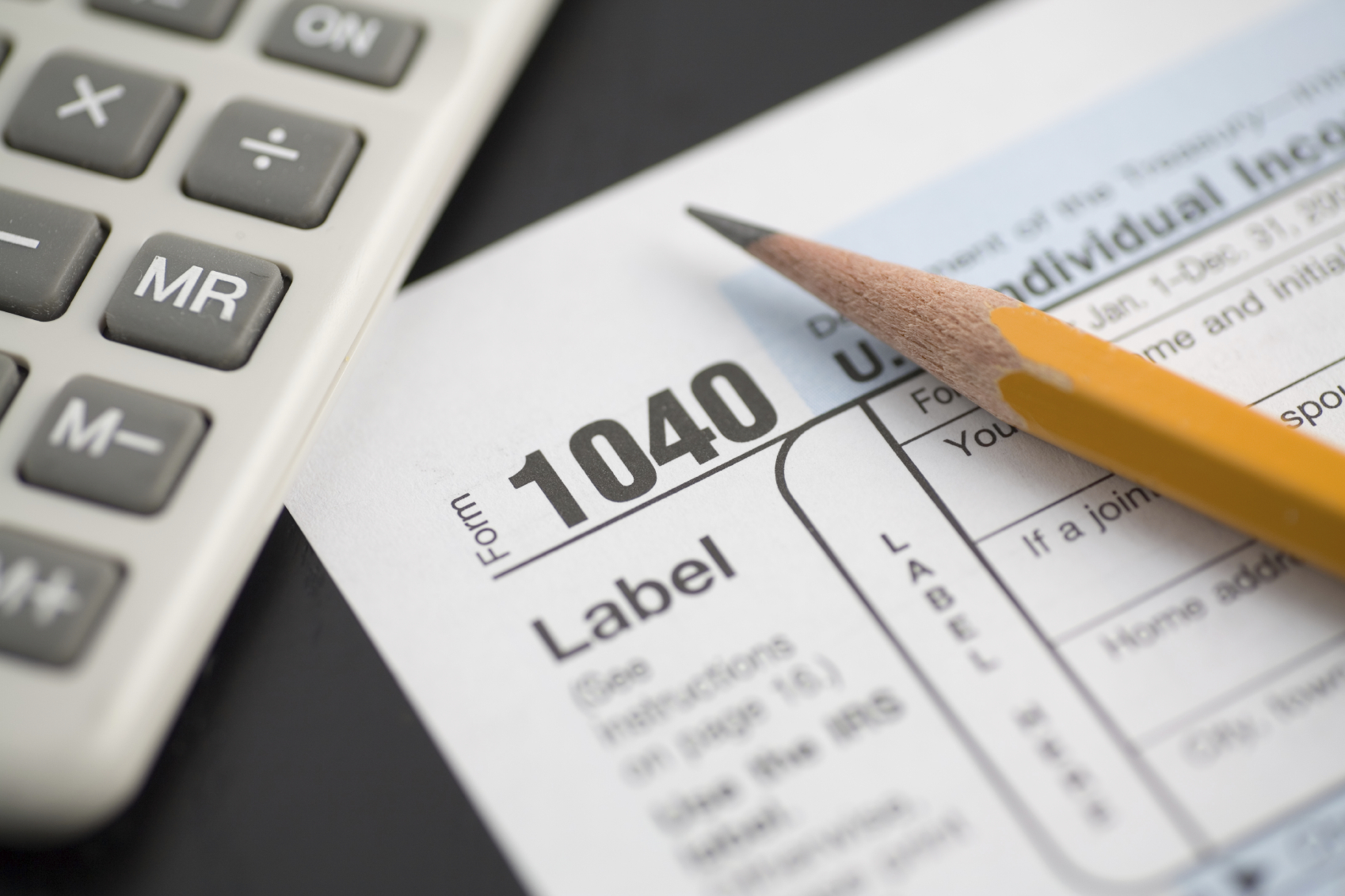 A tax form, pencil, and calculator close up.  Selective focus on "1040."